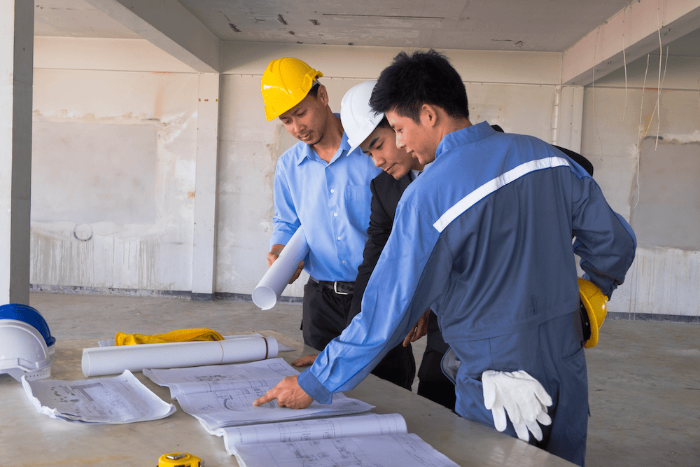 Three people in hard hats looking at plans.